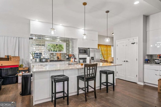 kitchen featuring white cabinetry, appliances with stainless steel finishes, decorative light fixtures, and dark hardwood / wood-style flooring