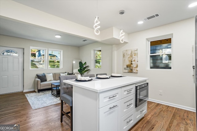 kitchen featuring a center island, dark hardwood / wood-style floors, built in microwave, decorative light fixtures, and white cabinetry