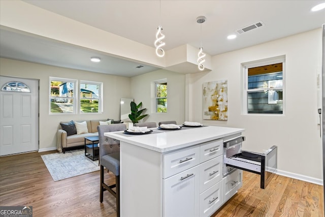 kitchen featuring a breakfast bar, decorative light fixtures, a center island, light hardwood / wood-style floors, and white cabinetry