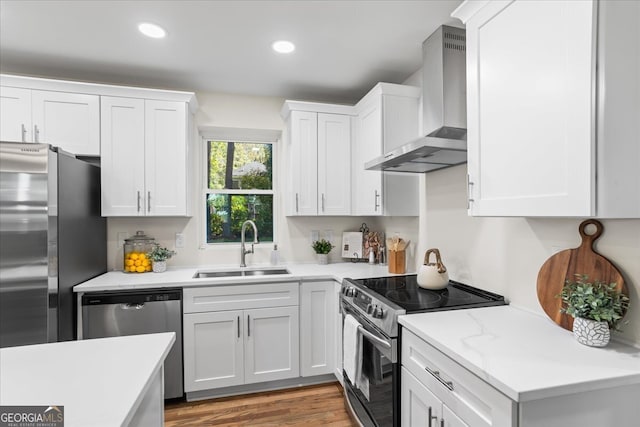 kitchen with white cabinetry, sink, wall chimney range hood, appliances with stainless steel finishes, and light wood-type flooring