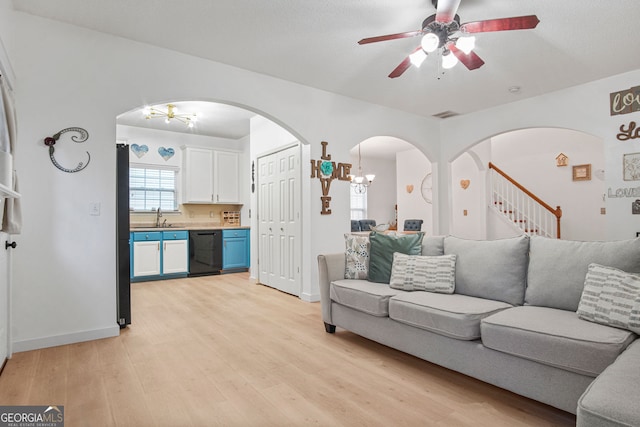 living room featuring light wood-type flooring, sink, and ceiling fan with notable chandelier