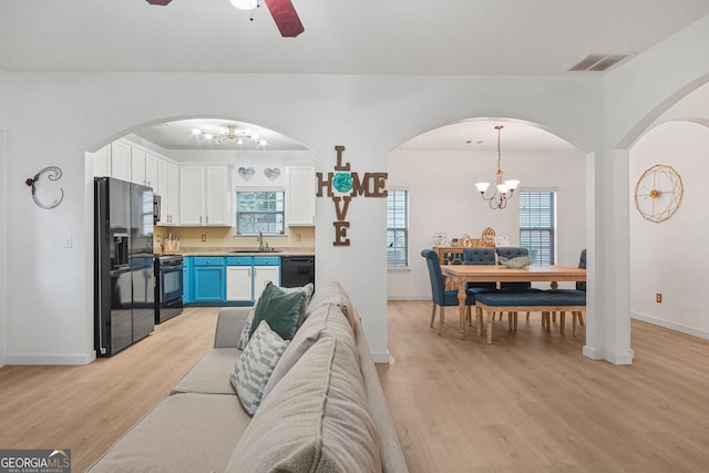 living room featuring ceiling fan with notable chandelier, sink, and light hardwood / wood-style flooring