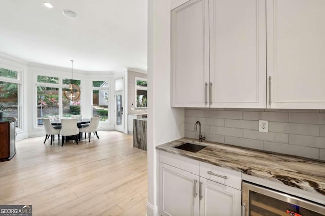 kitchen with light stone counters, pendant lighting, light hardwood / wood-style floors, white cabinets, and beverage cooler