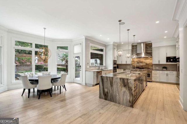 kitchen featuring light stone counters, wall chimney exhaust hood, hanging light fixtures, a spacious island, and white cabinetry