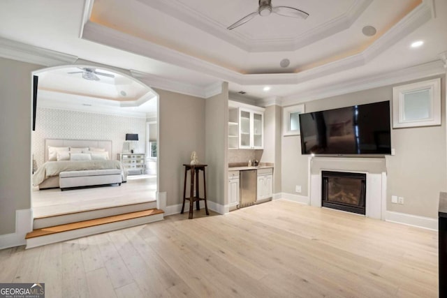 living room featuring crown molding, light hardwood / wood-style floors, ceiling fan, and a raised ceiling