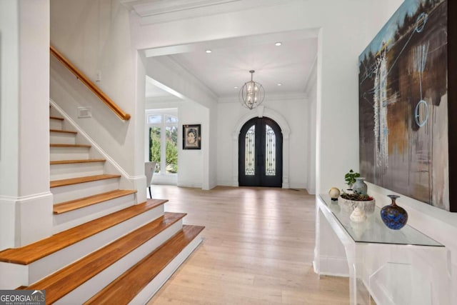 entrance foyer featuring light hardwood / wood-style floors, a chandelier, french doors, and ornamental molding