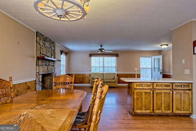 dining space featuring a fireplace, crown molding, dark hardwood / wood-style flooring, wooden walls, and ceiling fan