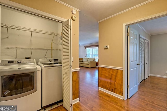 washroom featuring washing machine and clothes dryer, hardwood / wood-style flooring, and ornamental molding