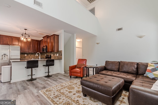 living room with a high ceiling, sink, an inviting chandelier, and light hardwood / wood-style flooring