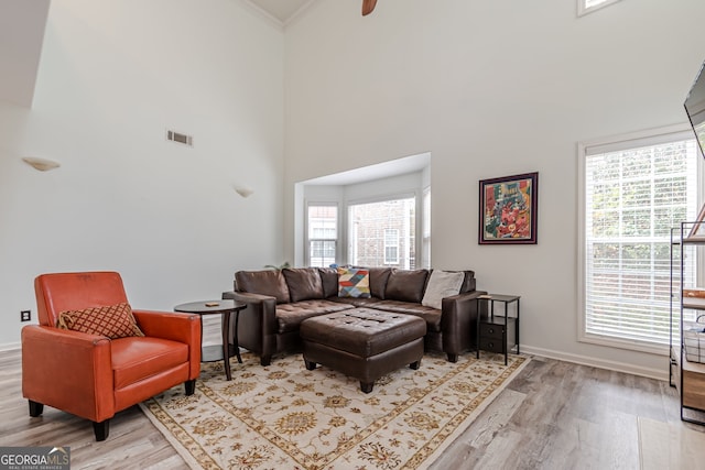 living room with crown molding, light hardwood / wood-style floors, and a towering ceiling