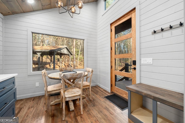 dining space featuring a notable chandelier, wood walls, wood finished floors, and baseboards