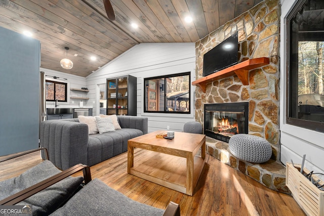 living room featuring vaulted ceiling, a stone fireplace, wooden ceiling, and wood finished floors