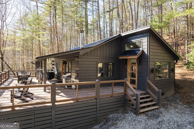 exterior space featuring board and batten siding, metal roof, a deck, and a view of trees