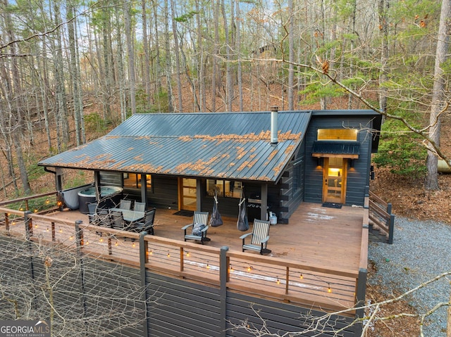 view of front of property featuring a forest view, an outdoor hot tub, metal roof, and a wooden deck