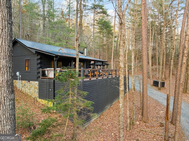 view of side of home with metal roof, crawl space, and a view of trees