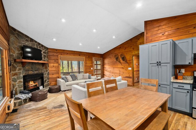 living room featuring light wood-type flooring, a stone fireplace, and wooden walls