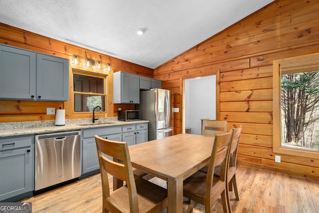 kitchen with wood walls, a sink, light wood-style floors, vaulted ceiling, and appliances with stainless steel finishes