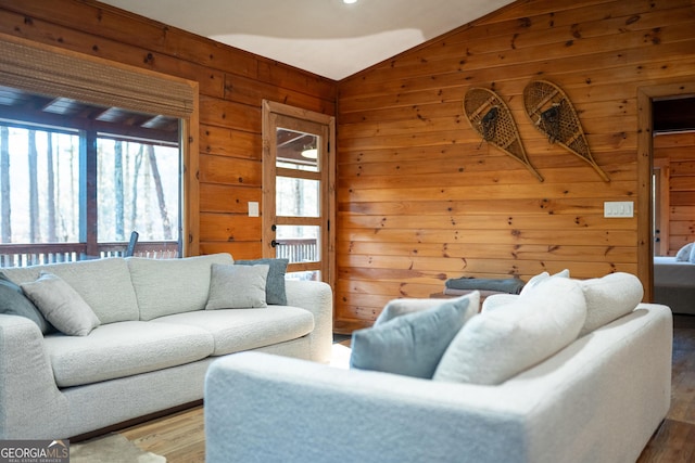 living room with vaulted ceiling, wooden walls, a stone fireplace, and light hardwood / wood-style floors