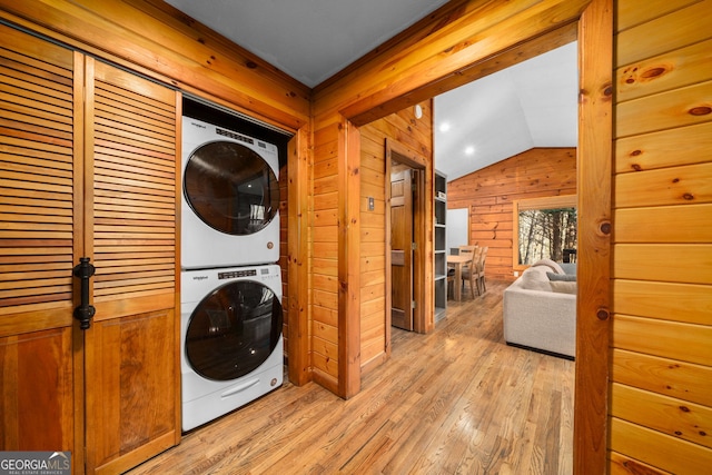 washroom featuring light wood-type flooring, stacked washer and clothes dryer, wooden walls, and laundry area