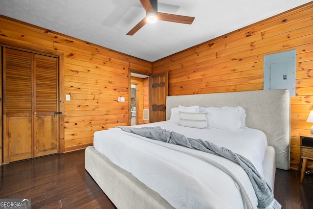 bedroom featuring a closet, dark wood-type flooring, ceiling fan, wooden walls, and electric panel