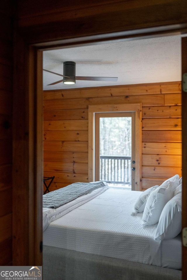 bedroom featuring a textured ceiling, ceiling fan, wood walls, and access to outside