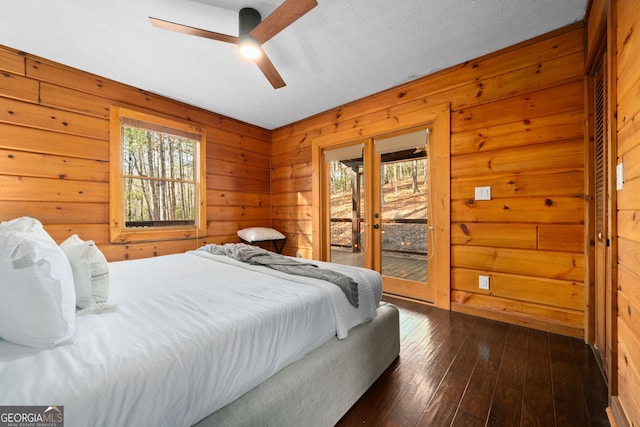 bedroom featuring dark wood finished floors, ceiling fan, access to outside, french doors, and wood walls