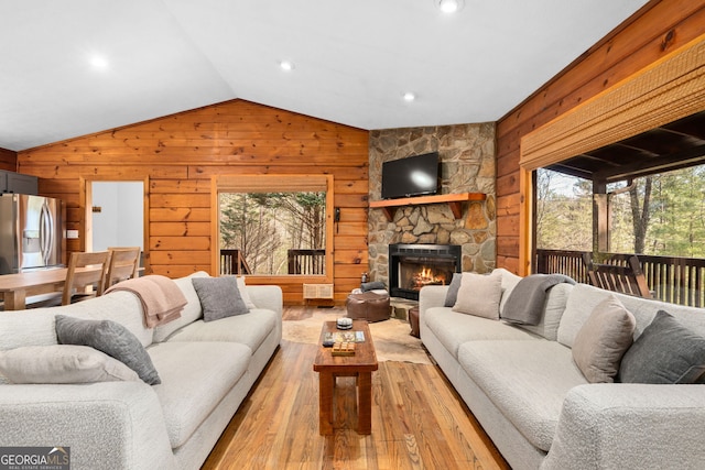 living area featuring a stone fireplace, light wood-style flooring, wooden walls, visible vents, and vaulted ceiling