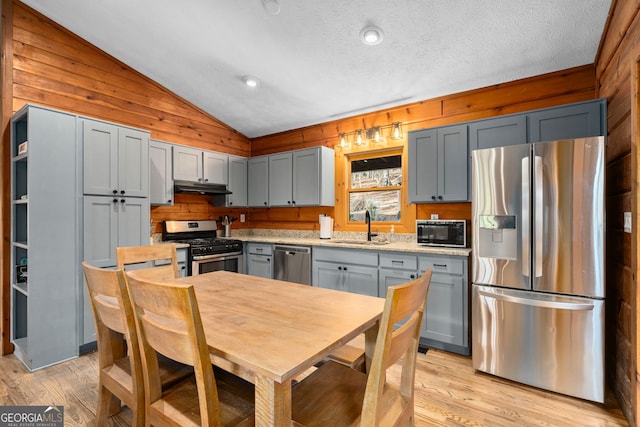 kitchen featuring stainless steel appliances, a sink, vaulted ceiling, light countertops, and light wood-type flooring