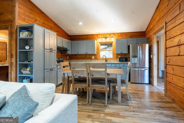 kitchen featuring wood walls, light stone counters, stainless steel appliances, and vaulted ceiling