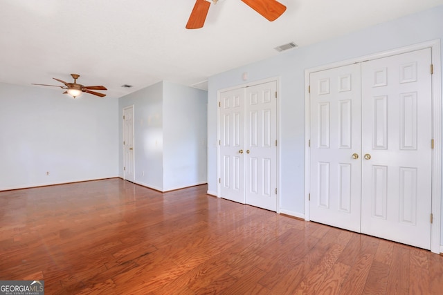 unfurnished bedroom featuring multiple closets, hardwood / wood-style flooring, and ceiling fan