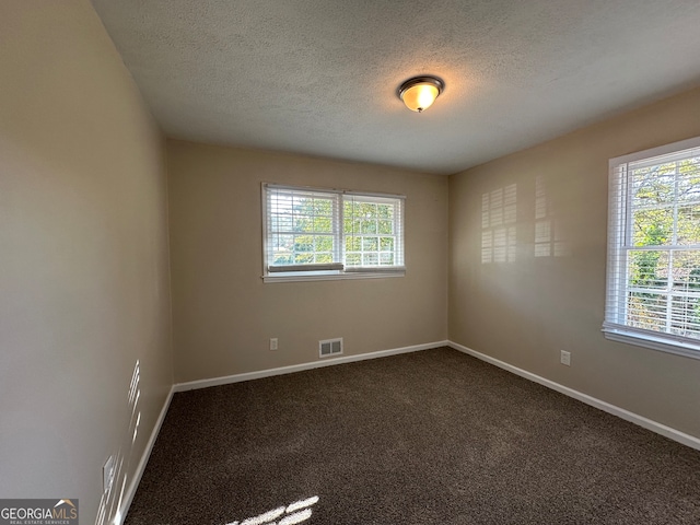 unfurnished room with a textured ceiling, dark colored carpet, and a healthy amount of sunlight