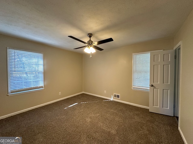 spare room featuring a textured ceiling, ceiling fan, and dark carpet