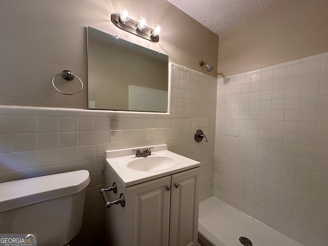 bathroom with toilet, tile walls, a textured ceiling, a tile shower, and vanity