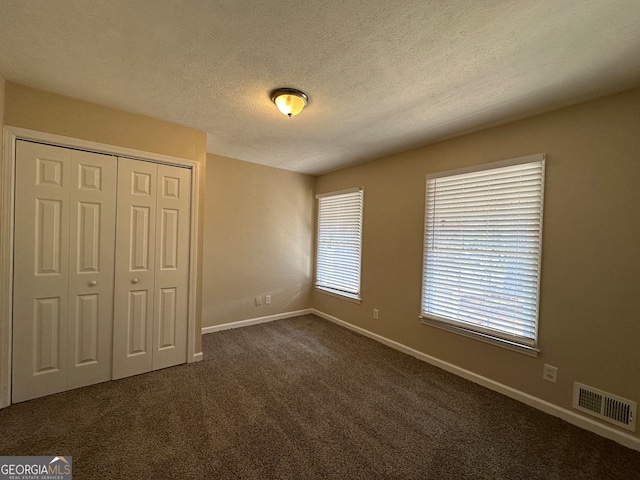 unfurnished bedroom with a closet, a textured ceiling, and dark carpet