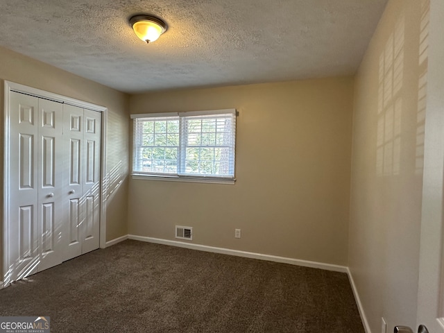 unfurnished bedroom with a closet, a textured ceiling, and dark colored carpet