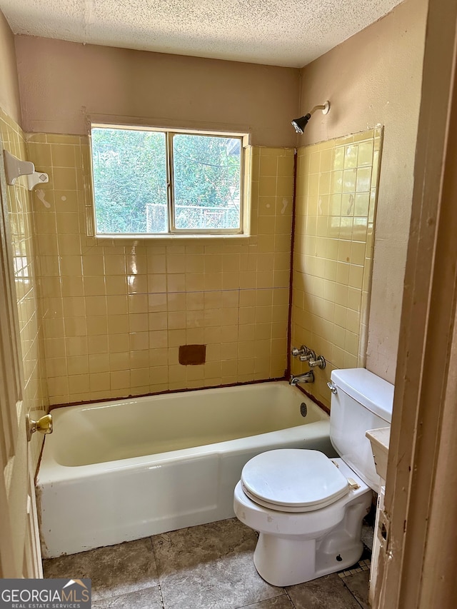 bathroom featuring tile patterned floors, tiled shower / bath, a textured ceiling, and toilet