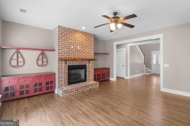 unfurnished living room featuring a brick fireplace, hardwood / wood-style floors, and ceiling fan