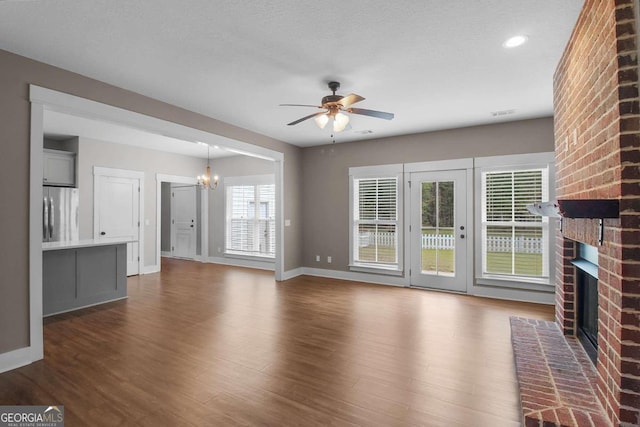 unfurnished living room featuring a brick fireplace, a healthy amount of sunlight, and dark wood-type flooring