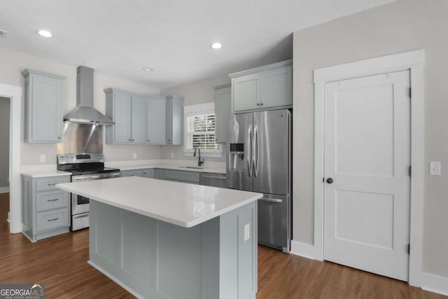 kitchen with dark wood-type flooring, a kitchen island, wall chimney range hood, and appliances with stainless steel finishes