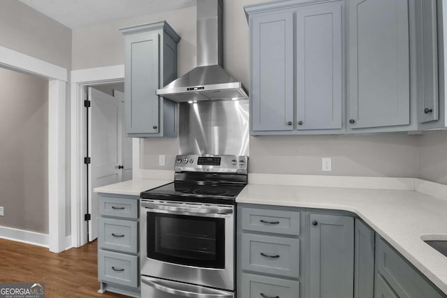 kitchen with gray cabinets, wall chimney range hood, stainless steel electric range oven, and dark hardwood / wood-style floors