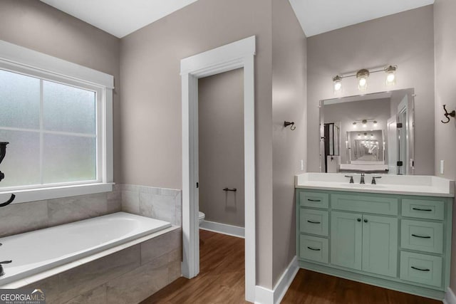 bathroom featuring tiled bath, hardwood / wood-style floors, vanity, and toilet