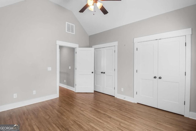 unfurnished bedroom featuring ceiling fan, wood-type flooring, multiple closets, and high vaulted ceiling