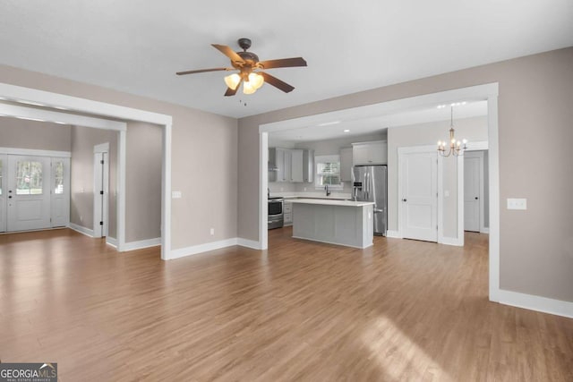 unfurnished living room featuring hardwood / wood-style floors, a wealth of natural light, and ceiling fan with notable chandelier