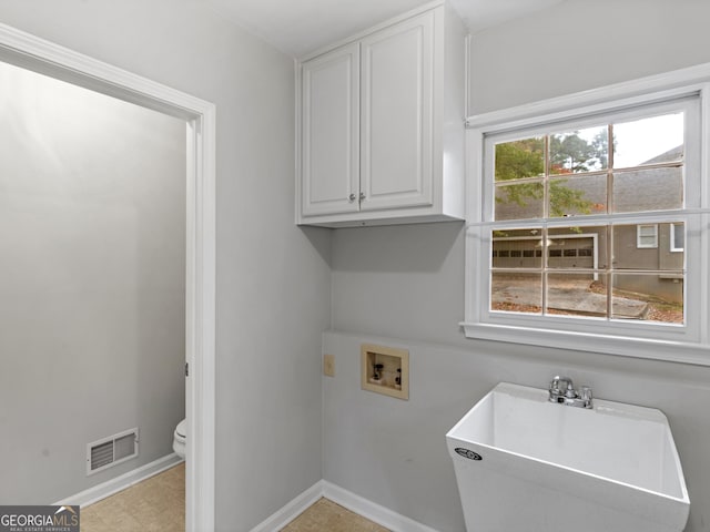 washroom featuring washer hookup, cabinet space, visible vents, a sink, and baseboards