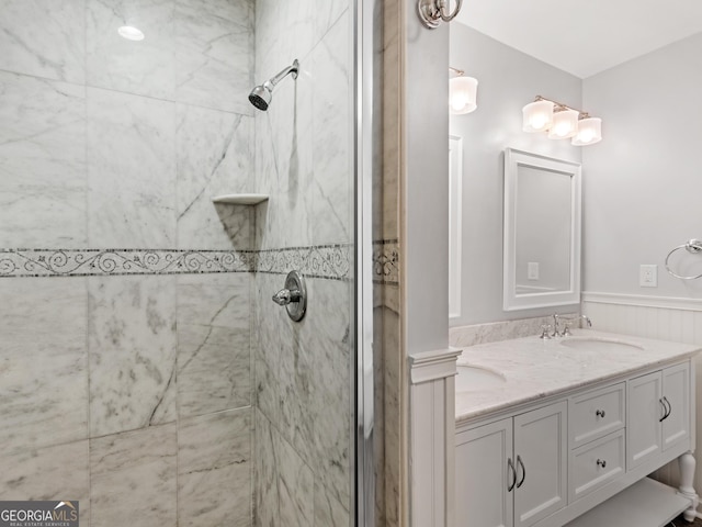 full bathroom with a wainscoted wall, double vanity, a sink, and a tile shower