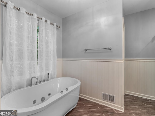 bathroom featuring wood finish floors, a jetted tub, wainscoting, and visible vents