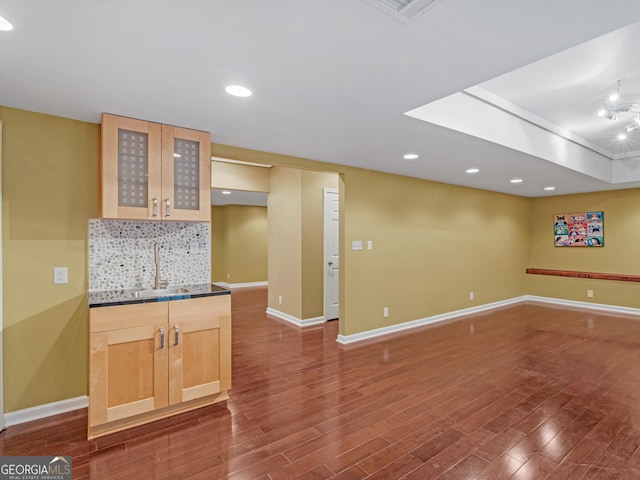 kitchen with dark wood finished floors, dark countertops, backsplash, glass insert cabinets, and a sink