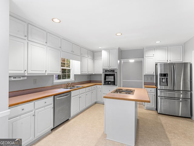 kitchen with butcher block counters, appliances with stainless steel finishes, white cabinetry, a kitchen island, and a sink