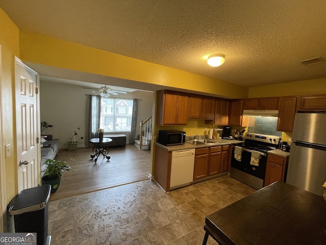 kitchen featuring appliances with stainless steel finishes, a textured ceiling, ceiling fan, sink, and light hardwood / wood-style flooring