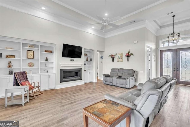 living room featuring ceiling fan with notable chandelier, a towering ceiling, crown molding, light wood-type flooring, and french doors